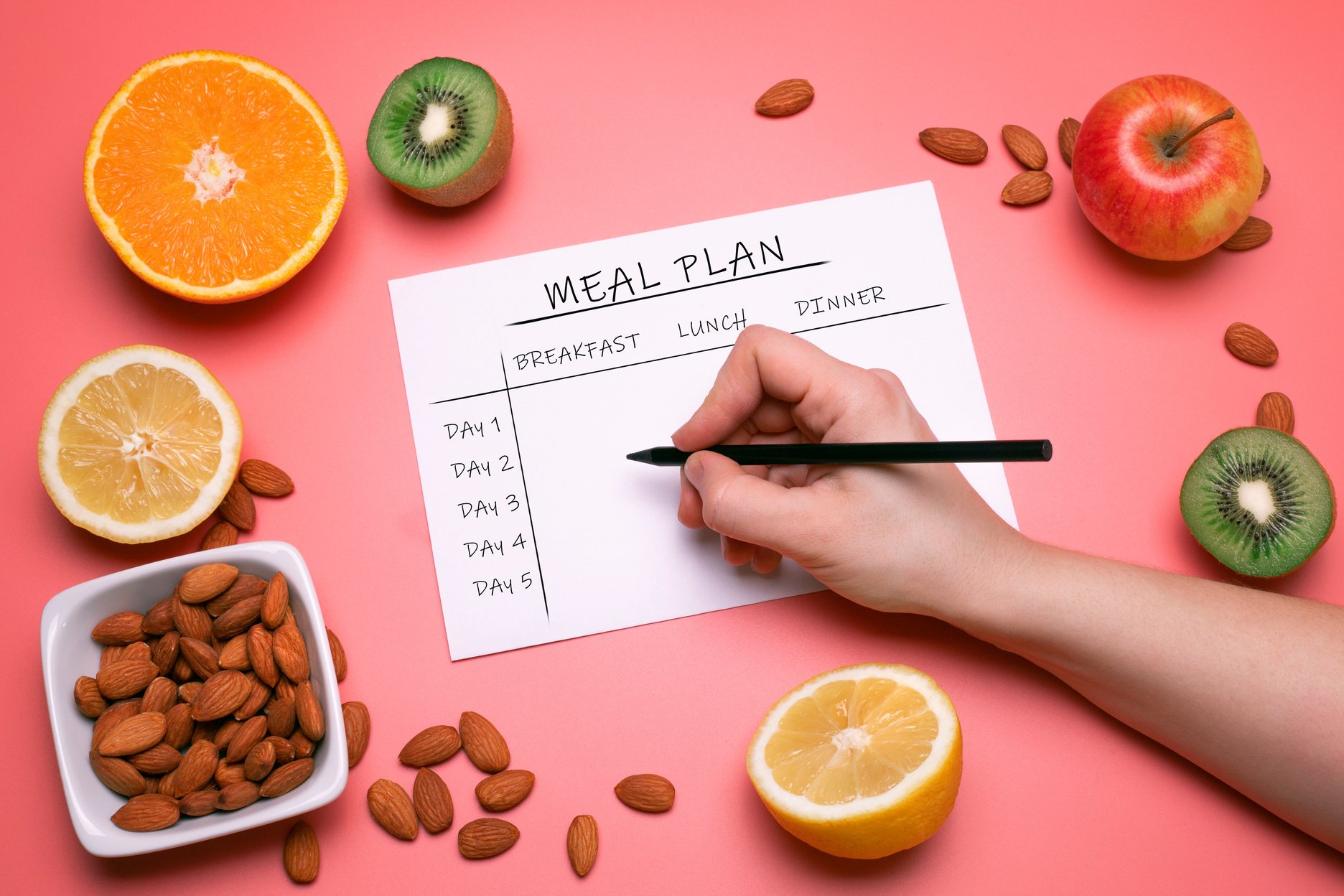 Calories control, meal plan, diet and weight loss concept. Top view of hand filling meal plan. Flat lay with various fruits and nuts on the pink background. Healthy food. Colorful design, high resolution product.