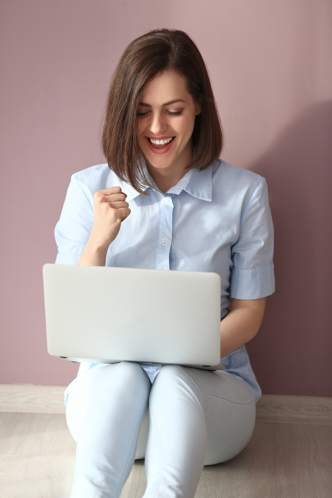 Happy Young Woman with Laptop Sitting near Color Wall